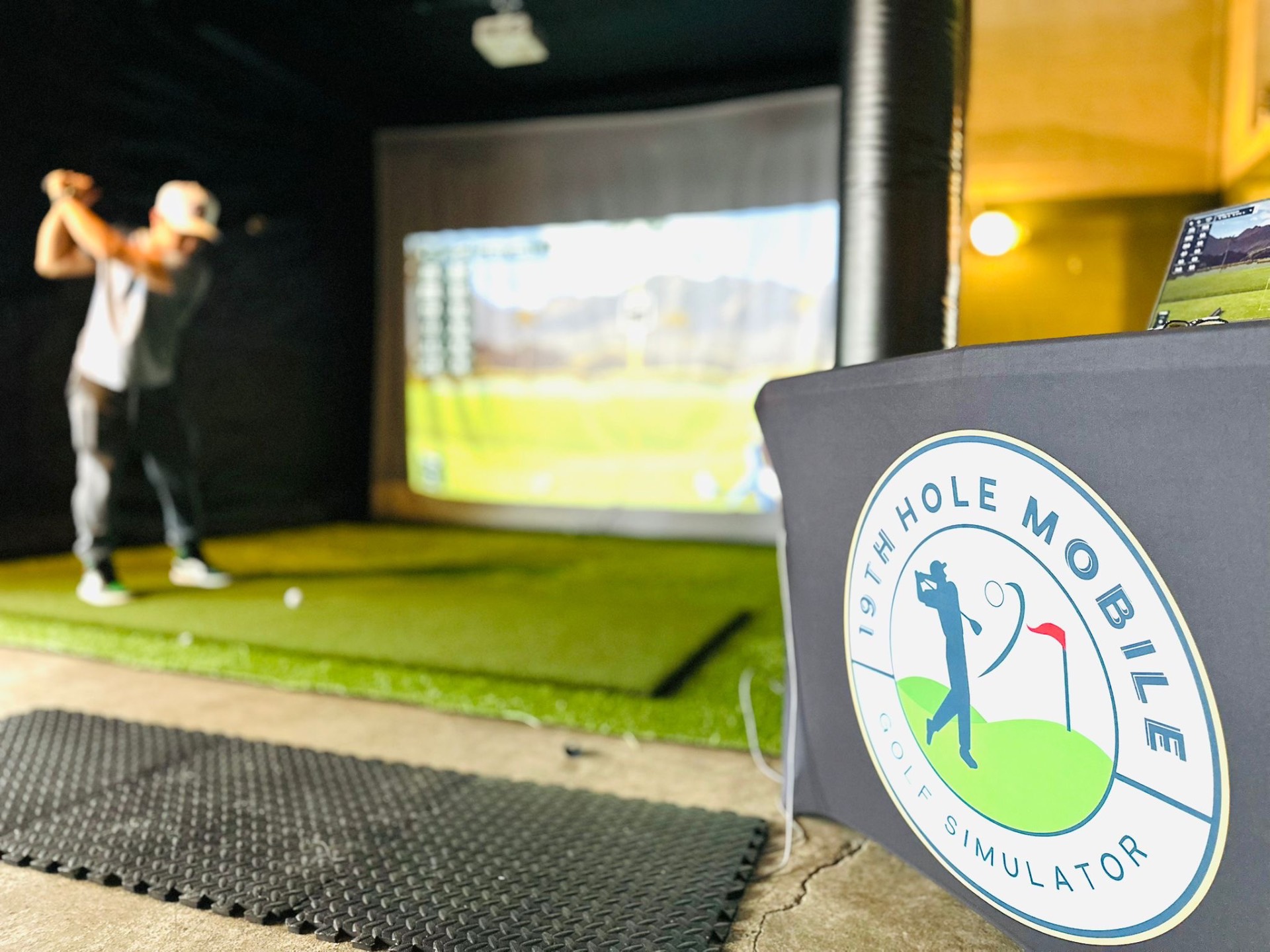 19th Hole Mobile Golf Simulator branded welcome table beside the simulator bay