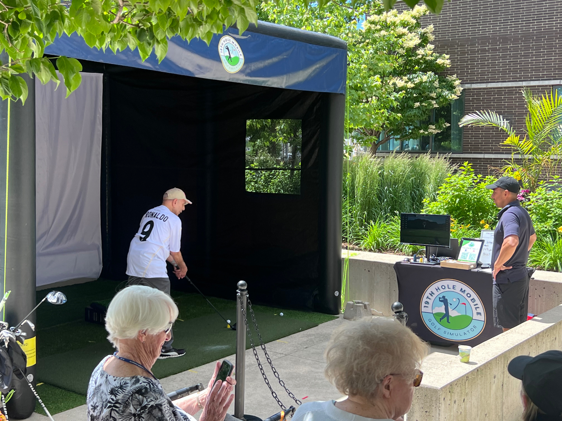 Guest teeing off inside the simulator bay while spectators watch at an outdoor residence event
