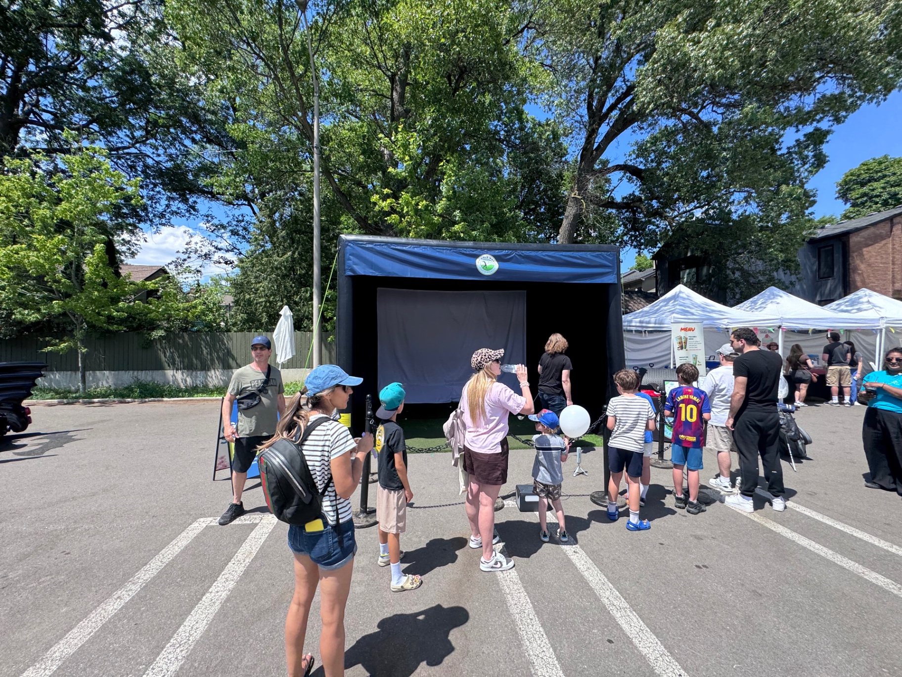 Families lined up at the mobile golf simulator during a closed-street summer festival