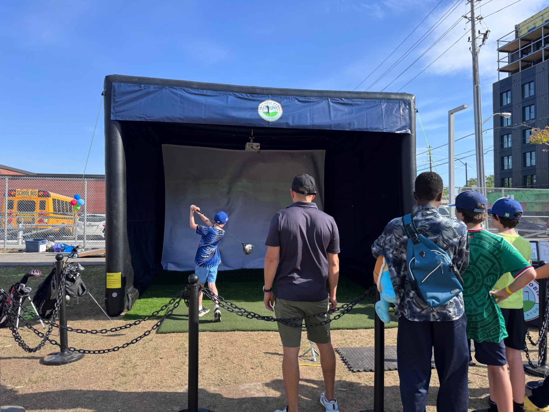 Families lined up to play the mobile golf simulator at an outdoor community festival