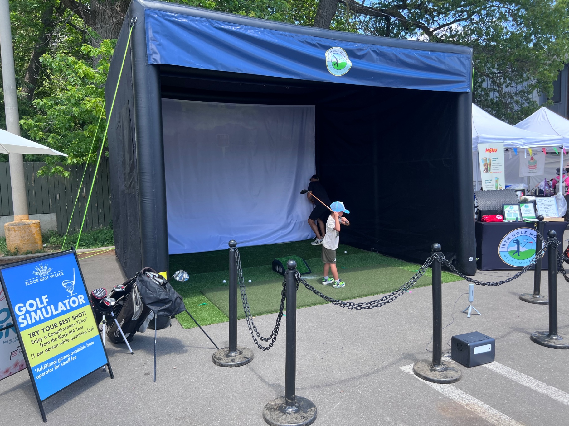 Mobile golf simulator staged on a closed street at a village festival with a young player
