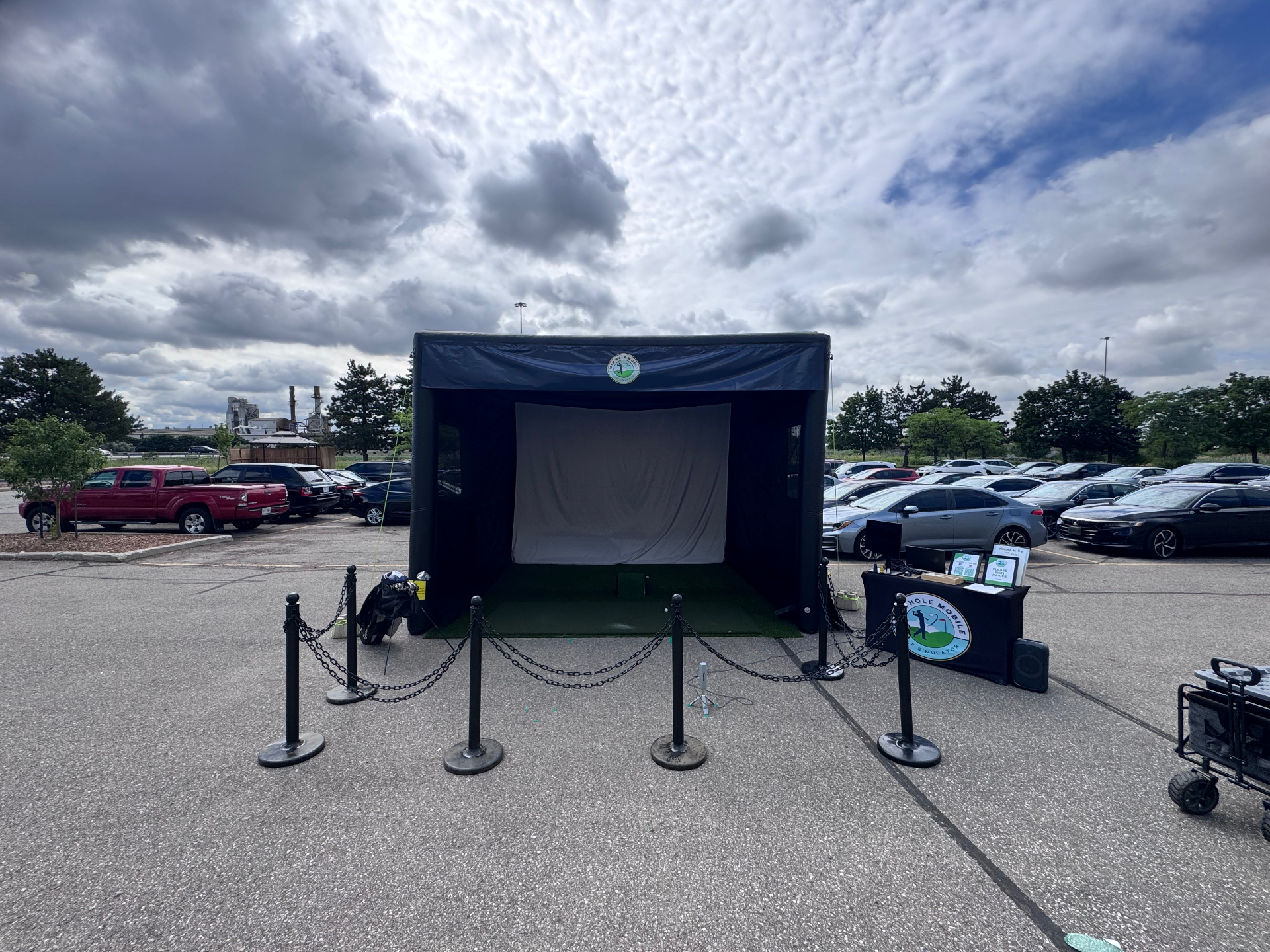 19th Hole Mobile simulator bay staged in a corporate parking lot with stanchions and a branded check-in table