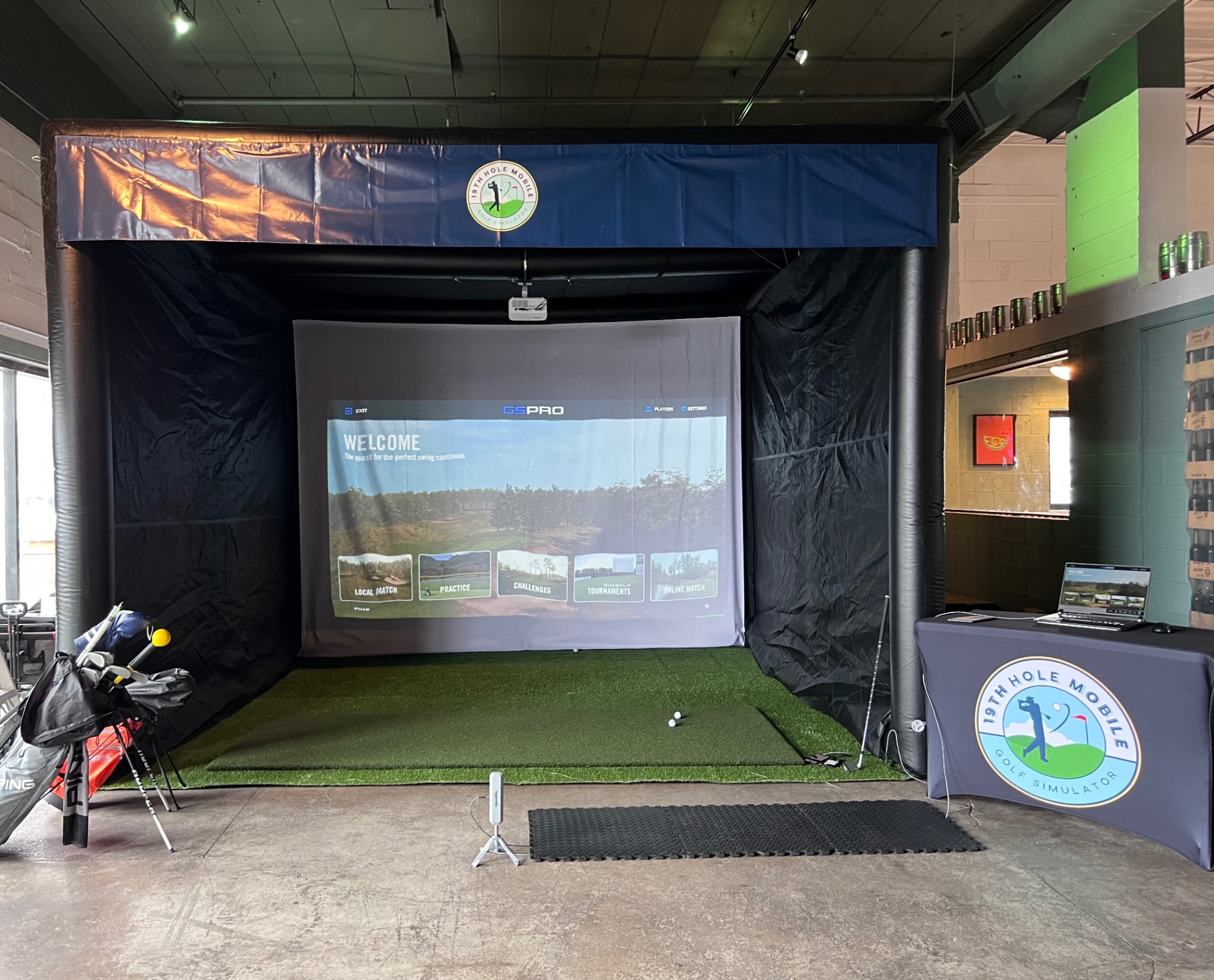 Full simulator bay with projection screen, turf hitting mat and clubs ready for play