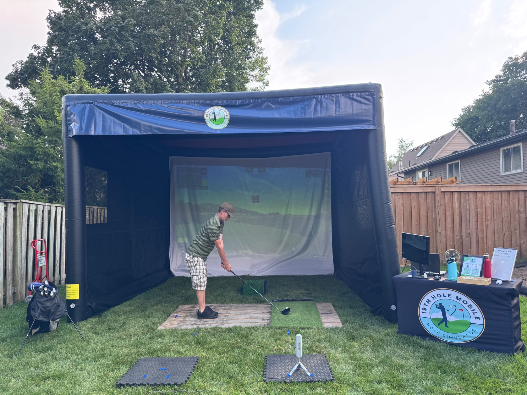19th Hole Mobile golf simulator set up in a backyard at dusk with a guest teeing off
